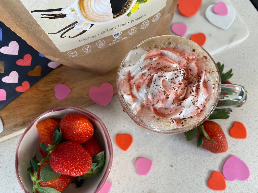 Pink strawberry sauce on whipped cream topped strawberry latte that is caffeine free. Bowl of strawberries and bag of Vanilla Nummy Creations Herbal Coffee Alternative.