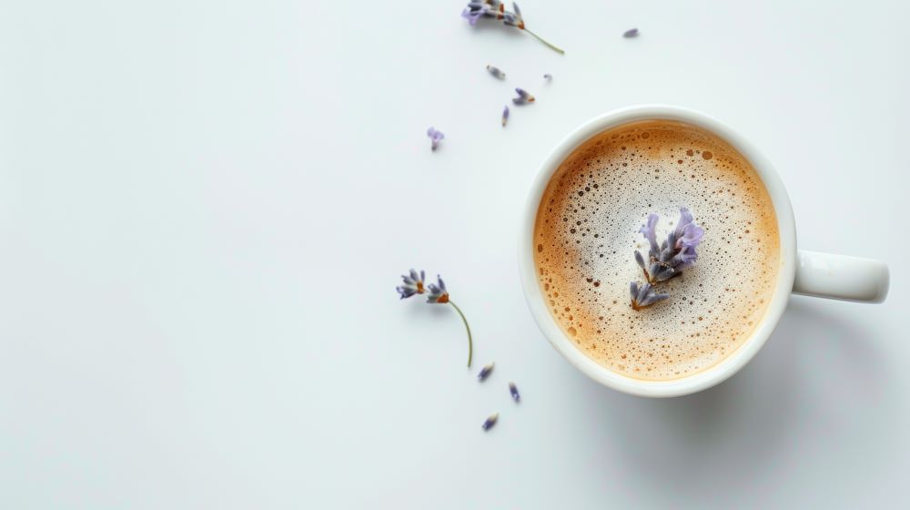 Cup of hot pretend coffee with Nummy Creations coffee alternative, with a jar of dried lavender flowers beside it. Lavender flowers scattered on counter 